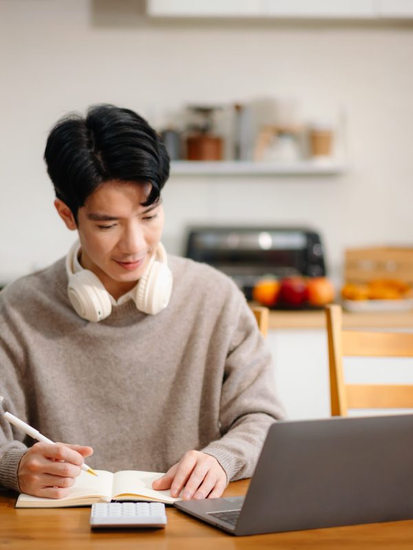Young Asian man with sitting working on laptops and tablets in a cozy workspace. Perfect for education, innovation, and remote work themes